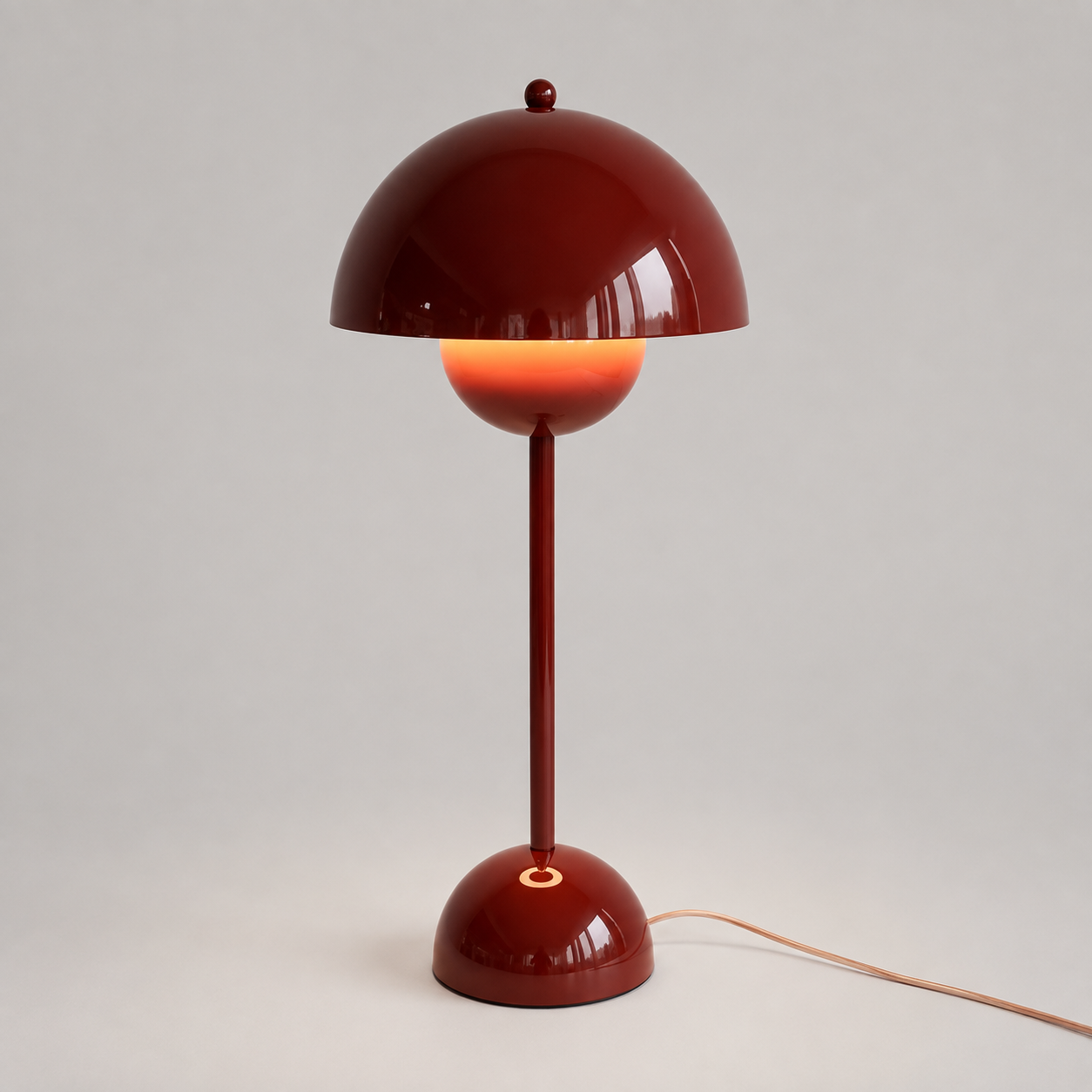 Red table lamp with a rounded dome shade, slim stem, circular base, power cord, and warm downward glow.