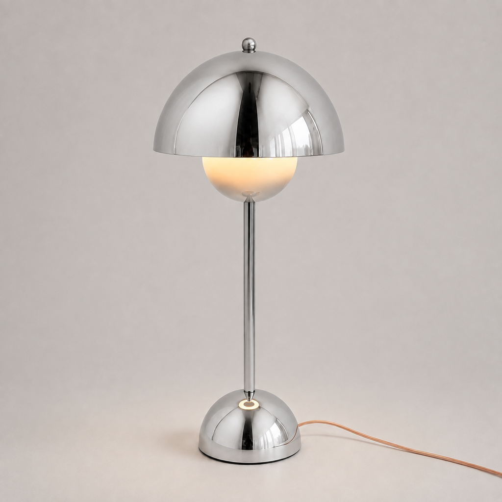 Silver table lamp with a reflective dome shade, slim stem, circular base, power cord, and warm downward glow.