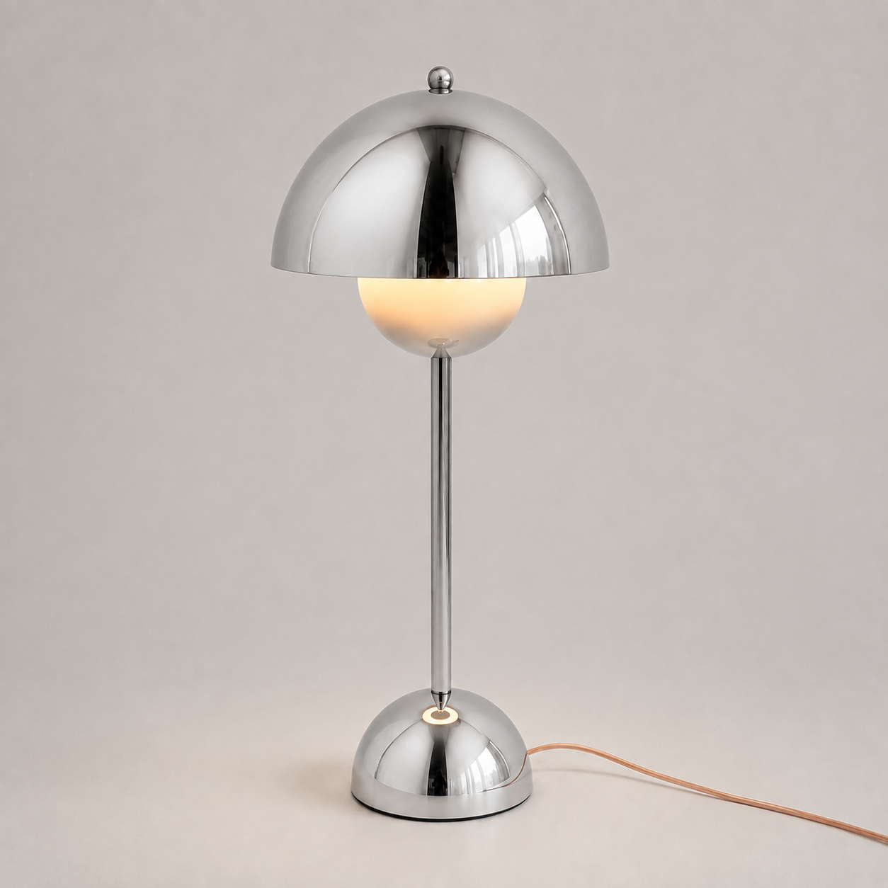 Silver table lamp with a reflective dome shade, slim stem, circular base, power cord, and warm downward glow.