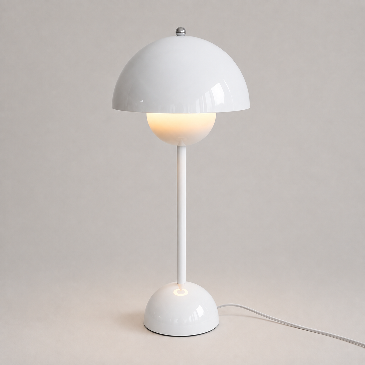 White table lamp with a rounded dome shade, slim stem, circular base, power cord, and warm downward glow.