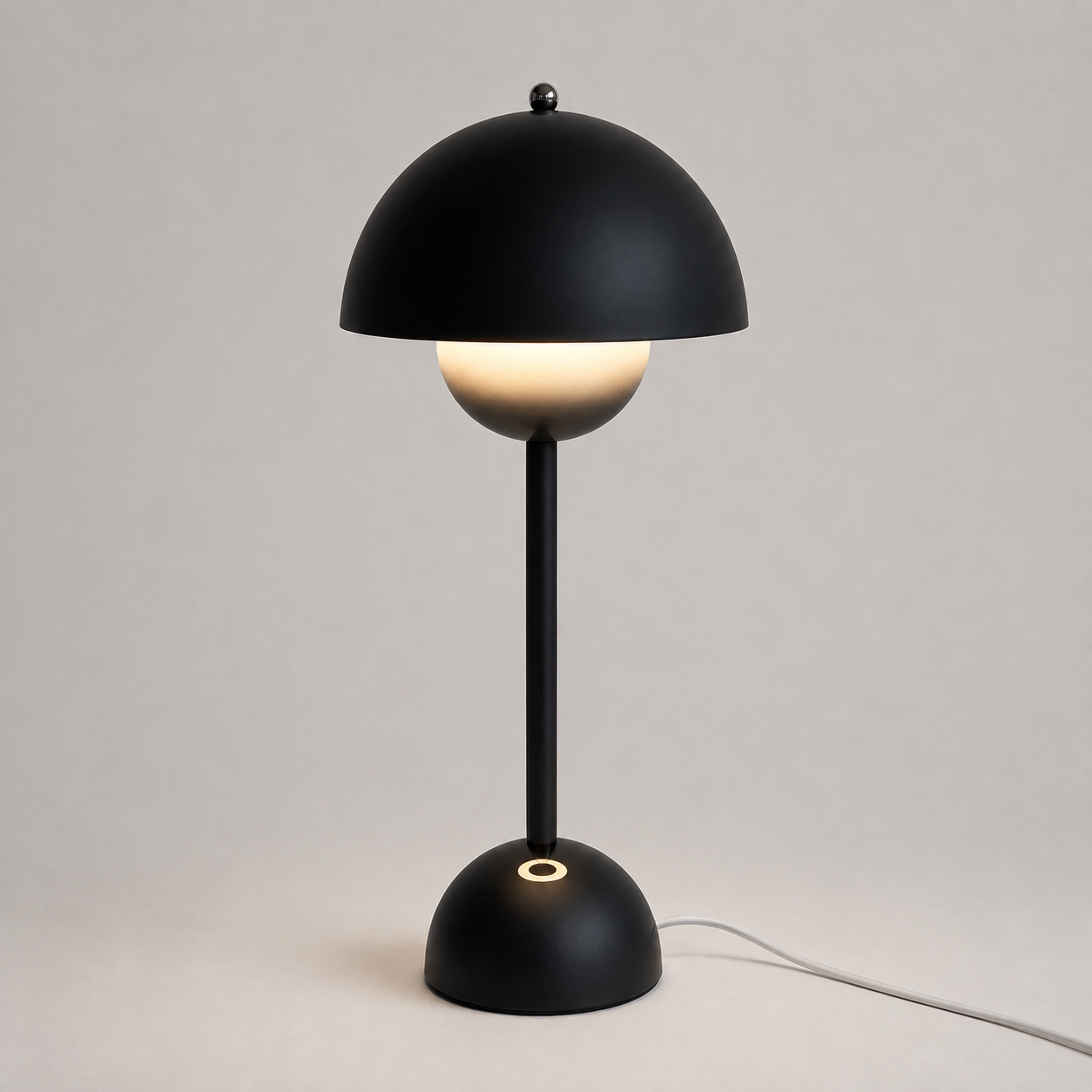 Black table lamp with a rounded dome shade, slim stem, circular base, power cord, and warm downward glow.