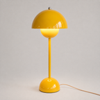 Yellow table lamp with a rounded dome shade, slim stem, circular base, power cord, and warm downward glow.
