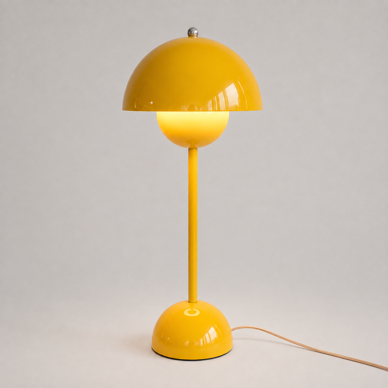 Yellow table lamp with a rounded dome shade, slim stem, circular base, power cord, and warm downward glow.