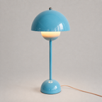 Blue table lamp with a rounded dome shade, slim stem, circular base, power cord, and warm downward glow.