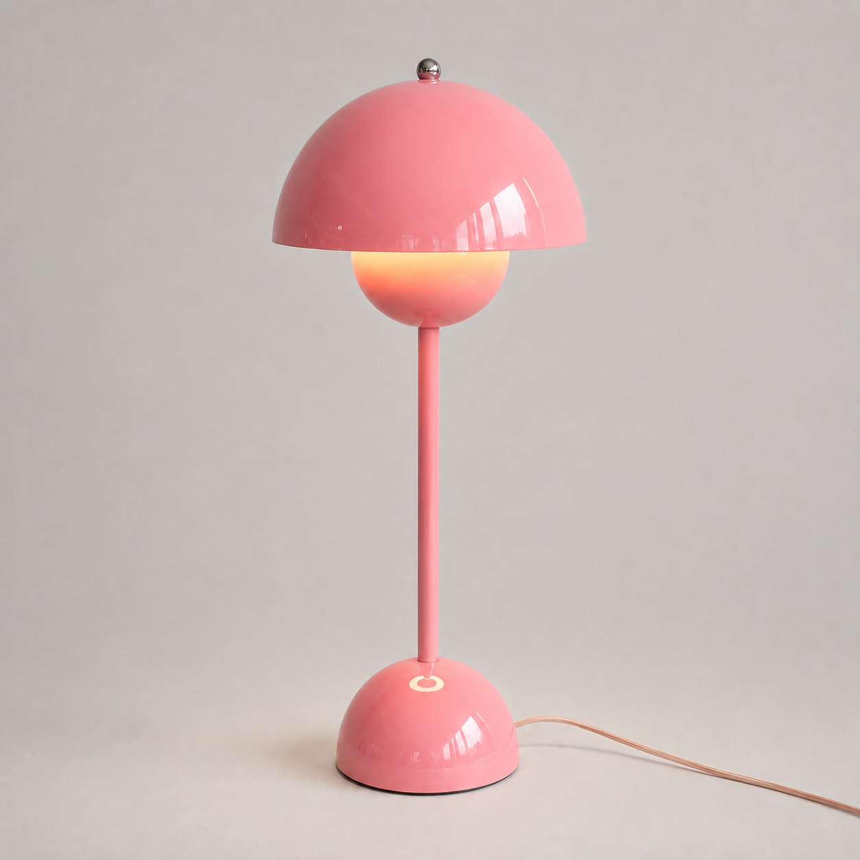 Pink table lamp with a rounded dome shade, slim stem, circular base, power cord, and warm downward glow.