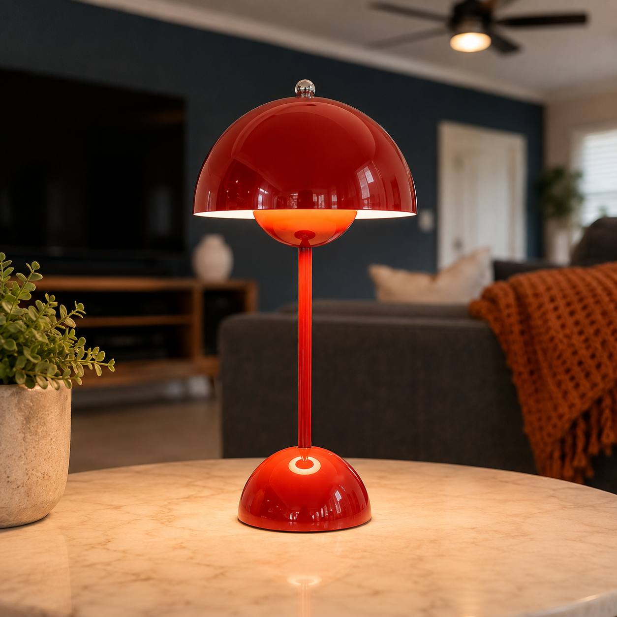 Red table lamp glowing on a round table in a dark living room with a sofa and potted plant.