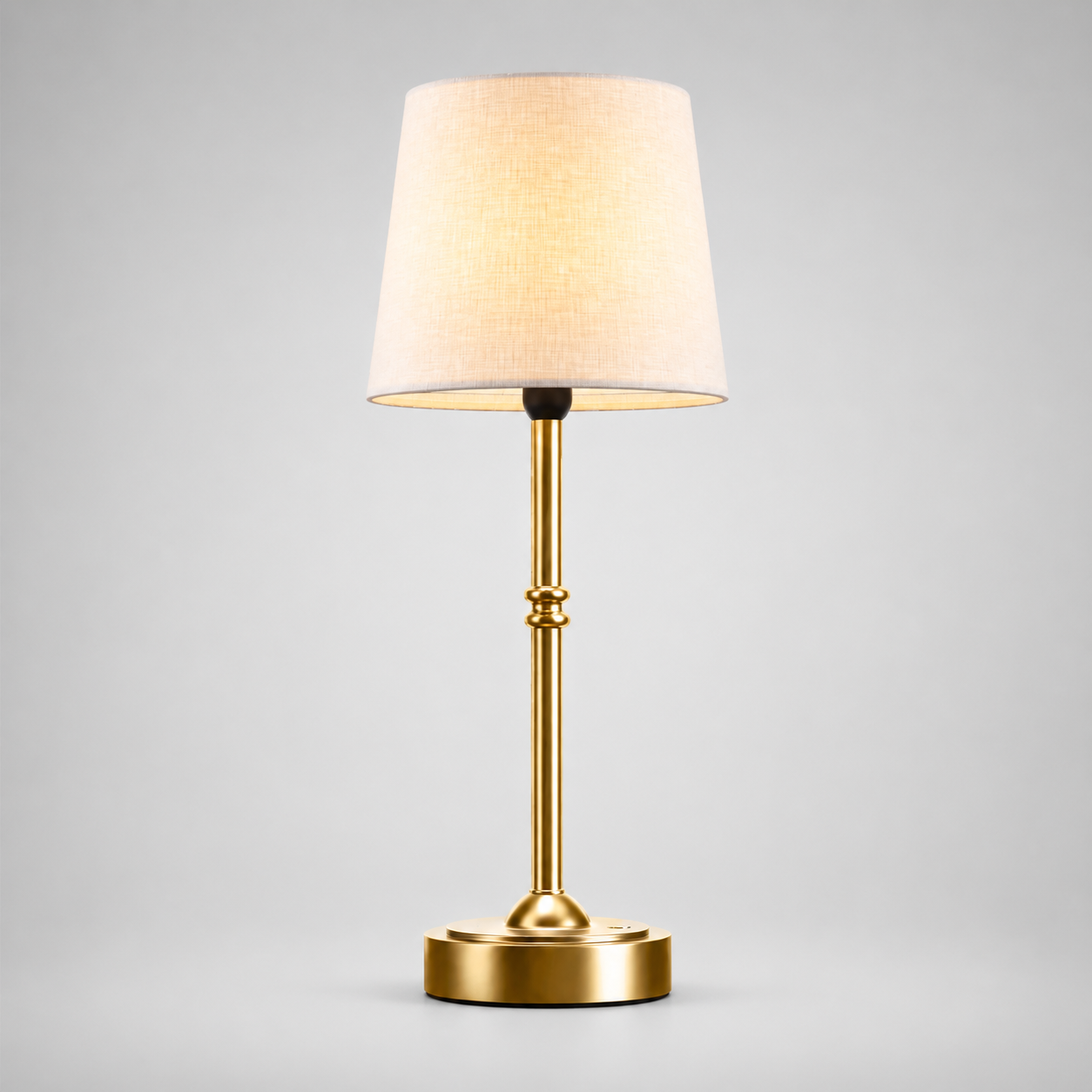 Gold cordless table lamp with a tapered white shade centered on a plain background.
