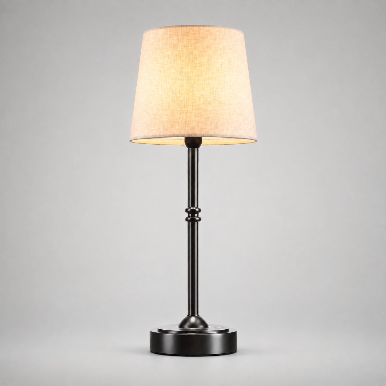 Black table lamp with a white fabric shade, illuminated against a light gray background.