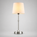 Silver table lamp with a white fabric shade, illuminated against a light gray background.