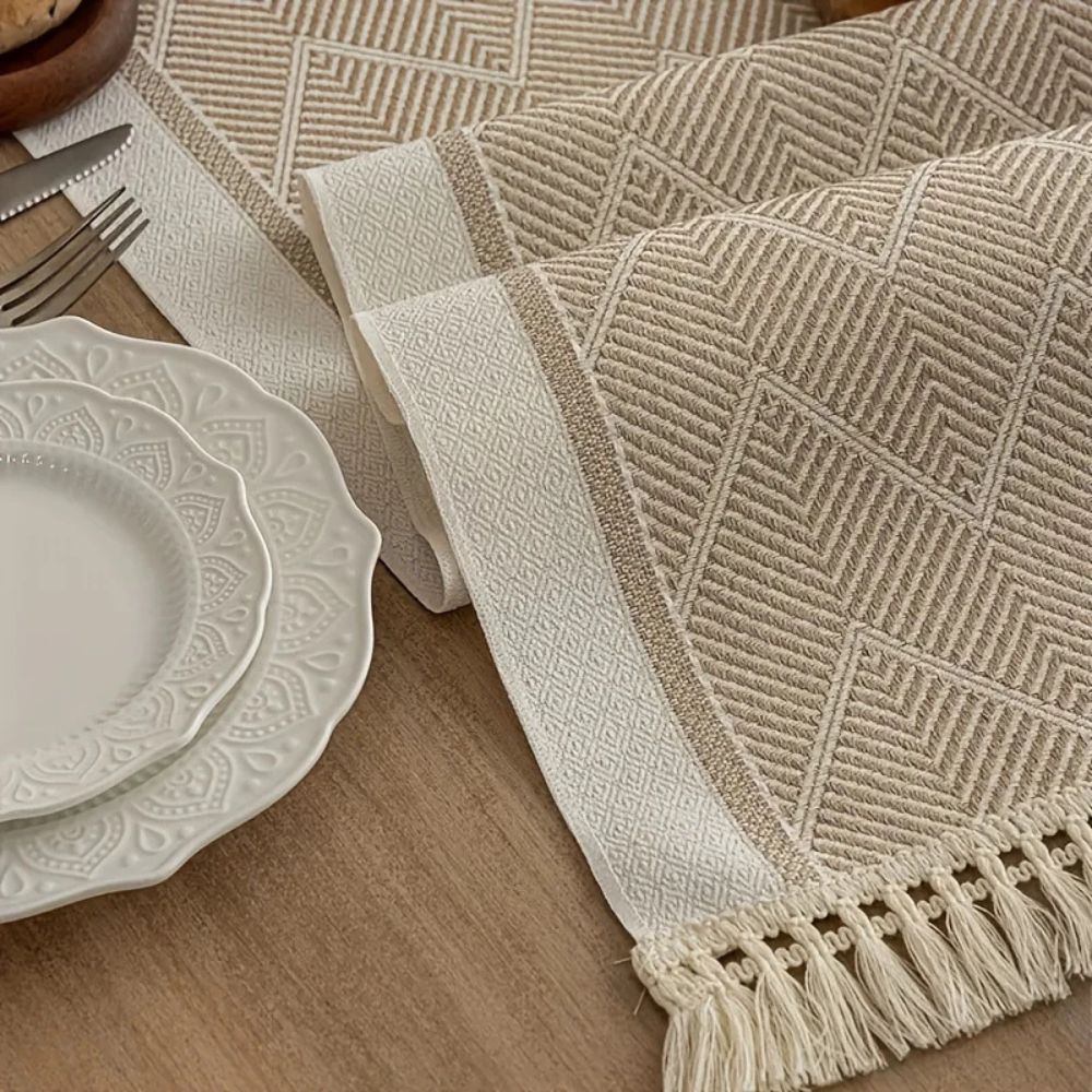 Beige table runner showing its woven zigzag texture and fringed edge.