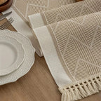 Beige table runner showing its woven zigzag texture and fringed edge.