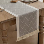 Gray table runner with a fringed edge draped over a wooden table.