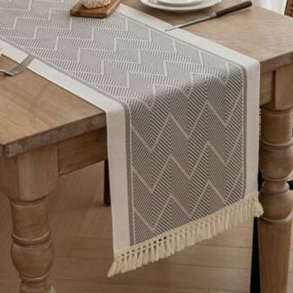Gray table runner with a fringed edge draped over a wooden table.