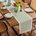 Green table runner with a zigzag pattern beneath glassware and flowers.