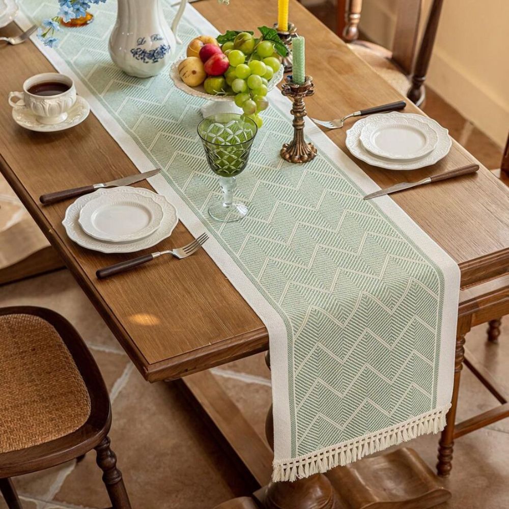 Green table runner with a zigzag pattern beneath glassware and flowers.