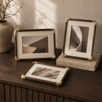 Three black walnut tabletop photo frames display neutral art on a dark wood cabinet.