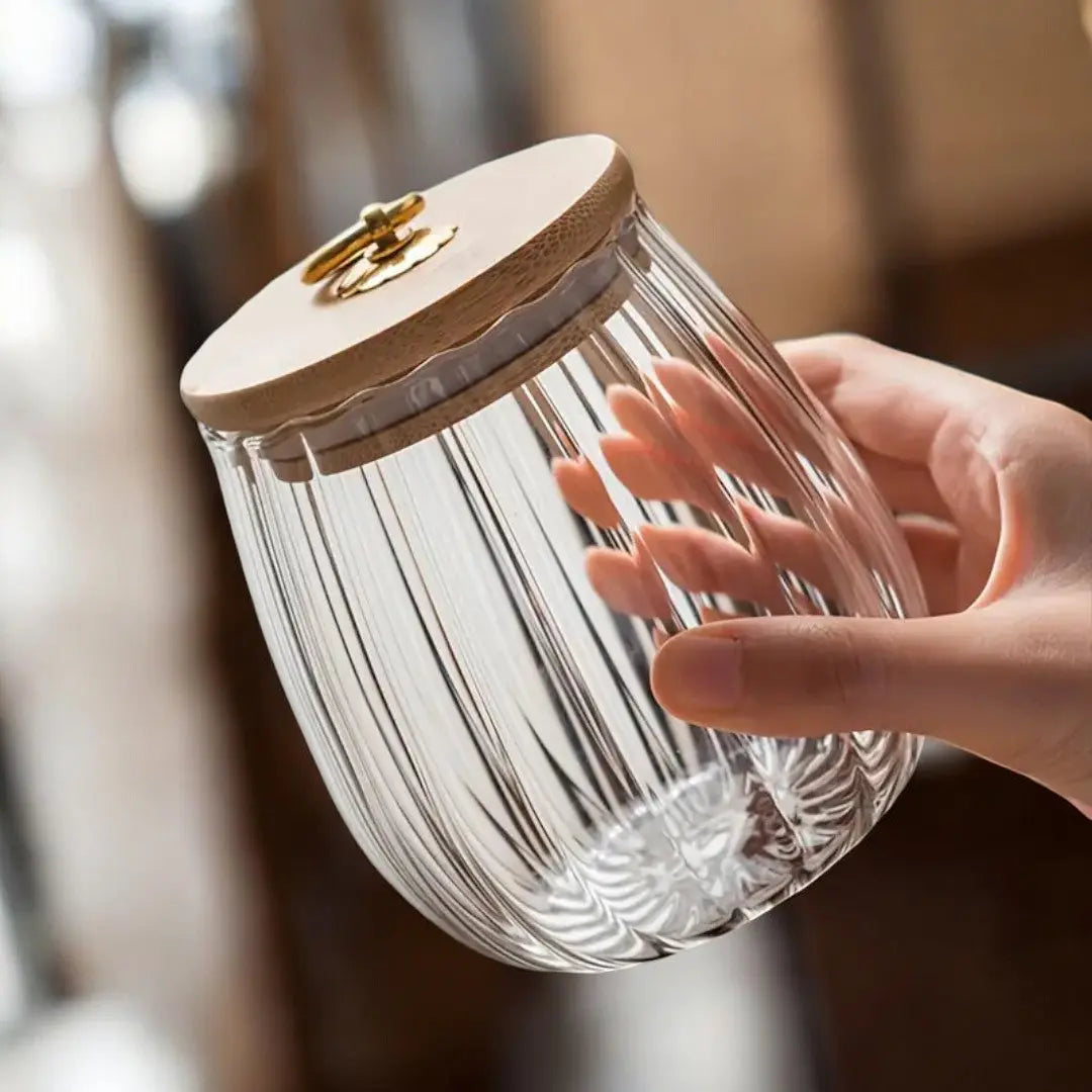 Round ribbed glass tea storage jar held in one hand with its wooden lid fitted
