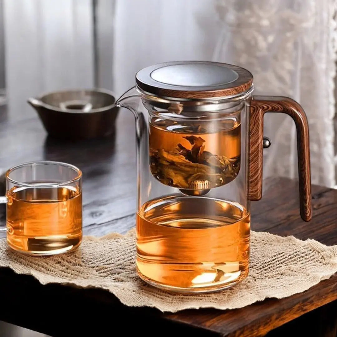 Glass teapot with loose tea in its inner chamber beside a cup