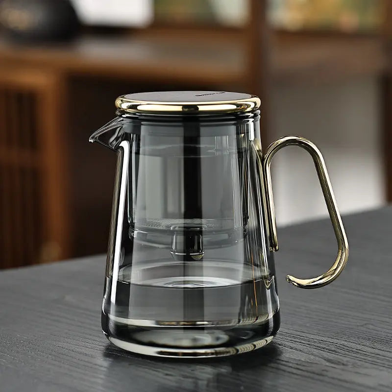 Glass teapot with gold toned handle and trim and an inner magnetic infuser