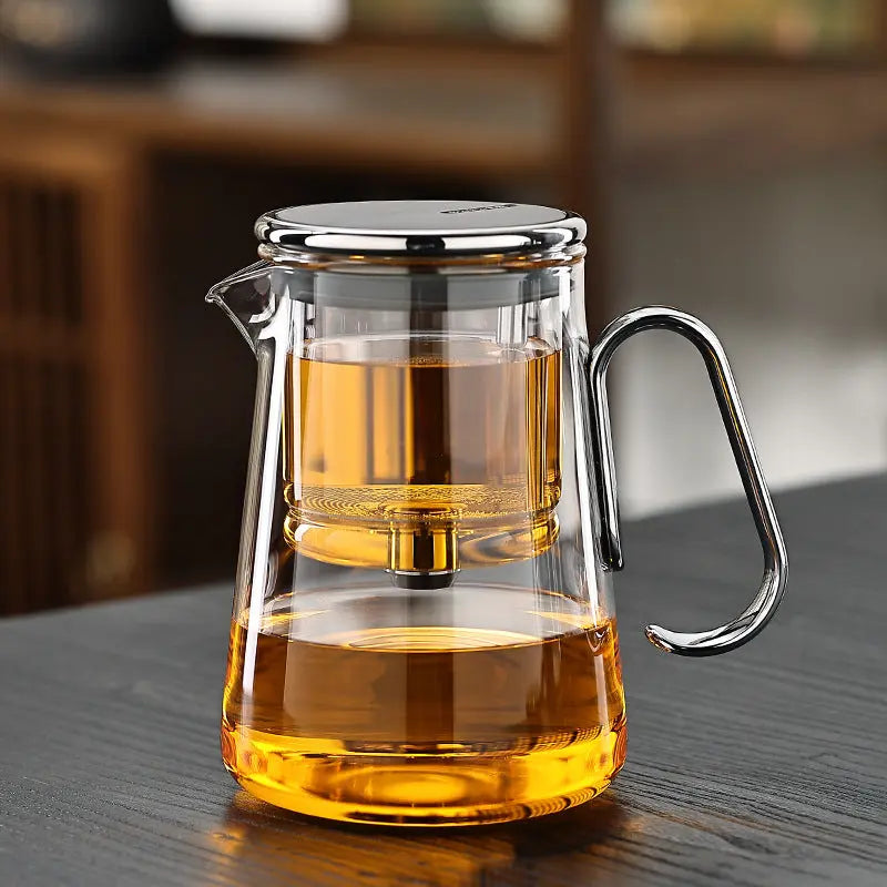 Glass teapot with silver toned handle and trim filled with amber tea