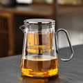 Glass teapot with silver toned handle and trim filled with amber tea