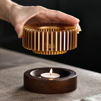 Hand lifting the slatted metal top above a lit tealight in the base.