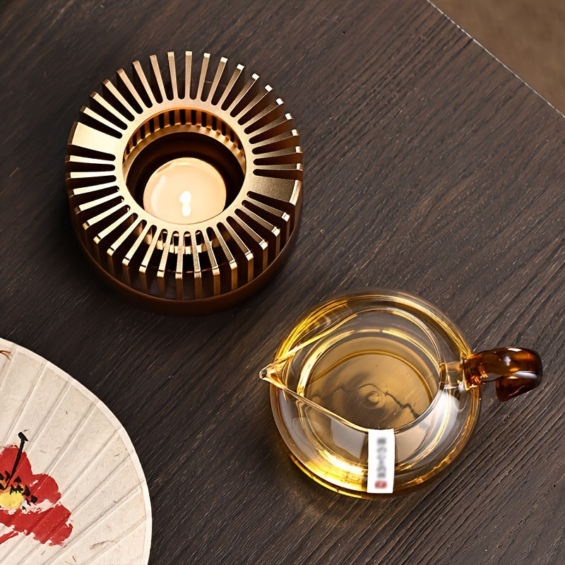 Overhead view of a gold tone warmer with a lit tealight and glass teapot.