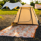 Boho floral throw blanket spread outside a tan camping tent on a sunny campsite
