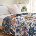 Artistic floral throw blanket spread across a bright bed with navy botanical border