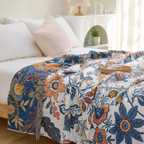 Artistic floral throw blanket spread across a bright bed with navy botanical border