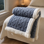 Sherpa fleece throw blanket in blue rolled and draped over a bed edge