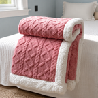 Sherpa fleece throw blanket in pink rolled and draped over a bed edge