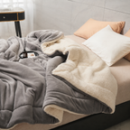 gray sherpa throw blanket with cream lining spread across a bed