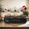 Black triple slow cooker with three raised glass lids on a holiday table