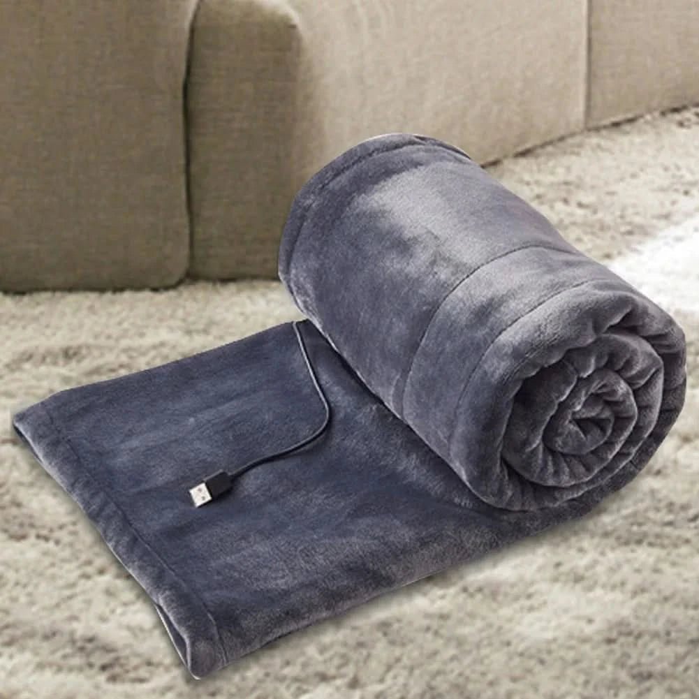 USB heated blanket in gray rolled beside a sofa with the USB cable visible.