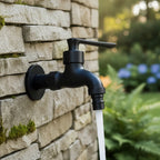 Wall-mounted faucet in matte black running water from a stone garden wall.