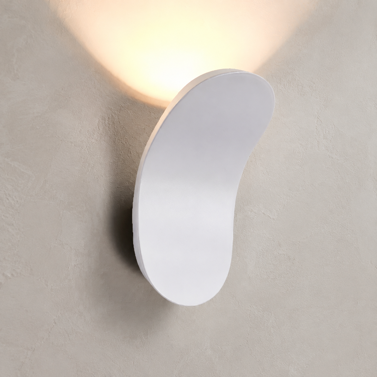 White curved wall sconce casting warm light on a greige plaster wall.