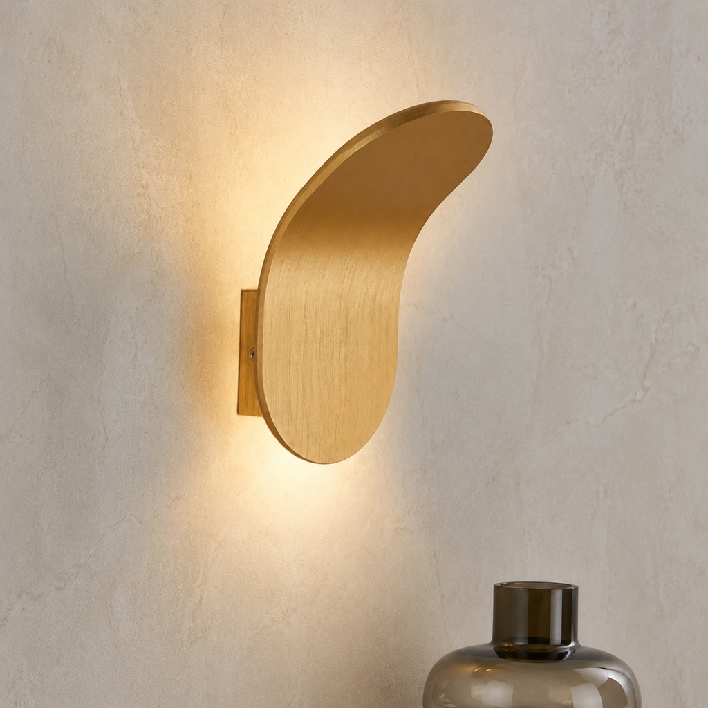 Gold curved wall sconce casting cool light on a pale plaster wall.