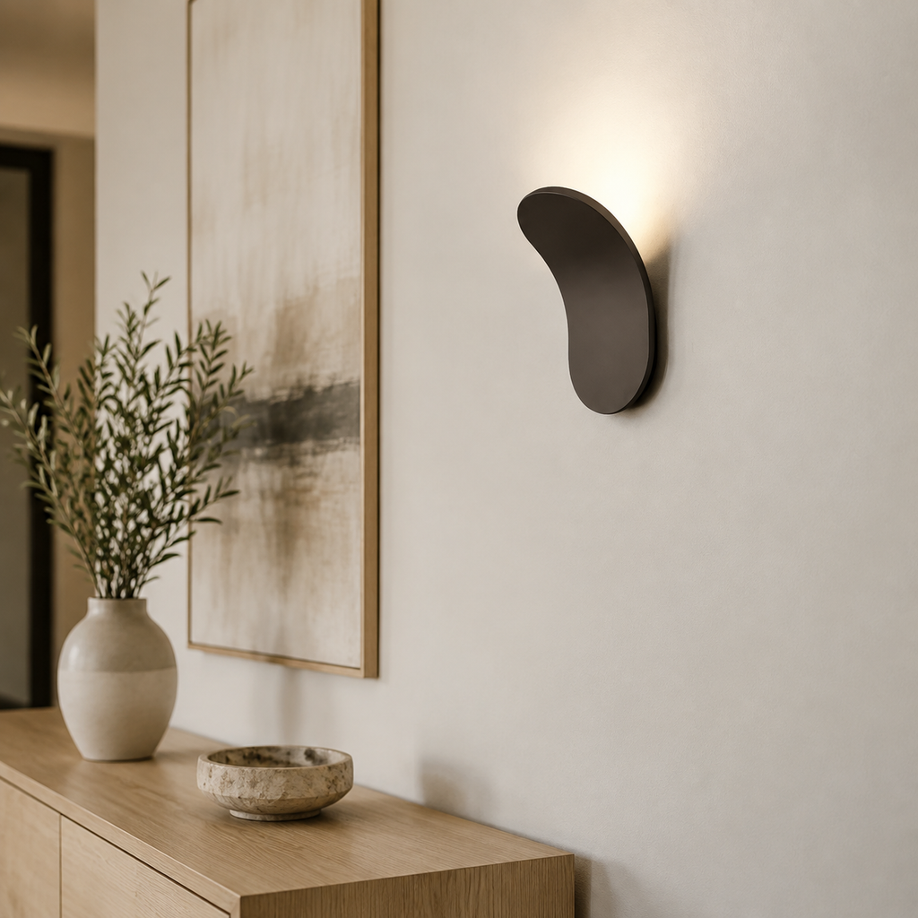Black curved wall sconce casting cool light above a dark console.