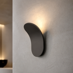 Gold curved wall sconce glowing warmly on a textured ivory wall.