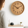 Wall clock with a natural wood face viewed by a woman in a living room.