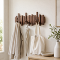 Walnut wall coat rack with folding piano key hooks holds a bag, umbrella, and light jacket.