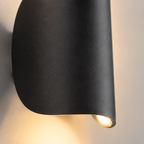 Close-up of a black wall sconce shade with warm light visible along the lower edge.