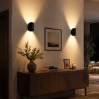 Two black wall sconce fixtures glow above a console table with framed art and a vase.