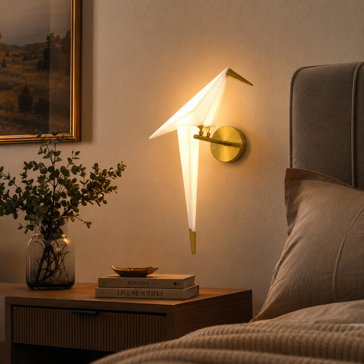 Origami bird LED wall lamp glowing warm white above a wooden bedside table with books and a glass vase.