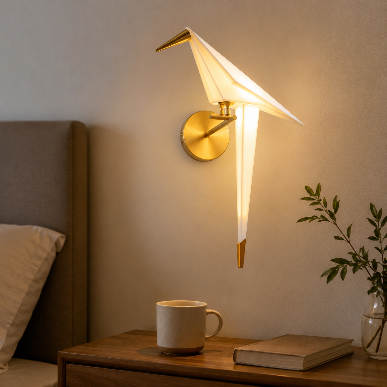 Origami bird LED wall lamp glowing warm white above a wooden bedside table with a mug, book, and plant.