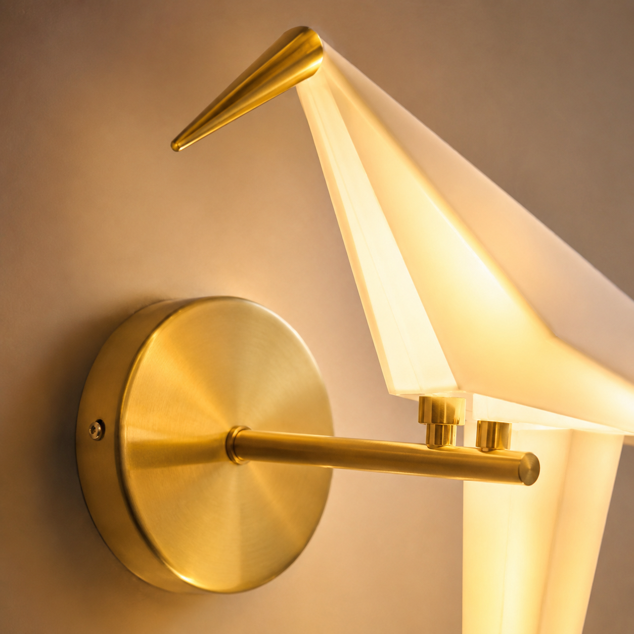 Close-up of an illuminated origami bird LED wall lamp with a translucent acrylic shade and brushed gold mounting plate.