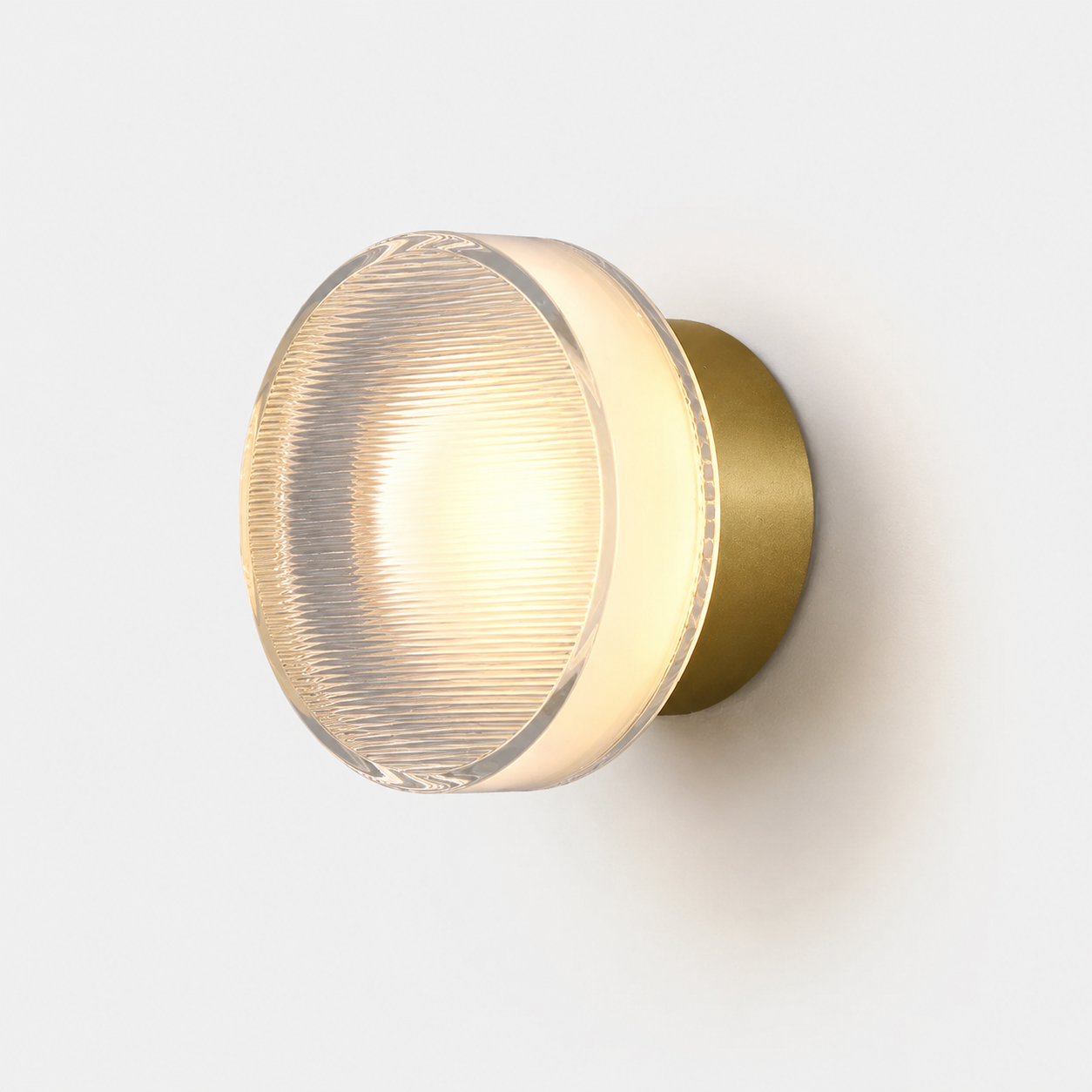 Round ribbed acrylic LED wall lamp glowing warm white with a brass mounting base against a white wall.