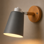 Adjustable cone wall lamp with a solid wood mounting base, glowing warm white against a neutral wall. 