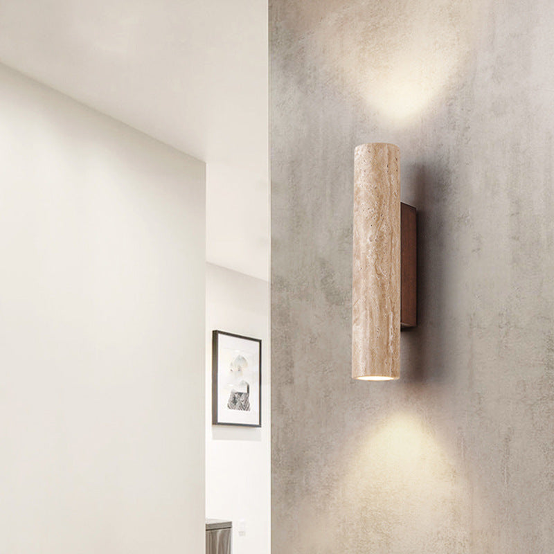 Cylindrical travertine wall sconce casting light above and below its natural stone shade